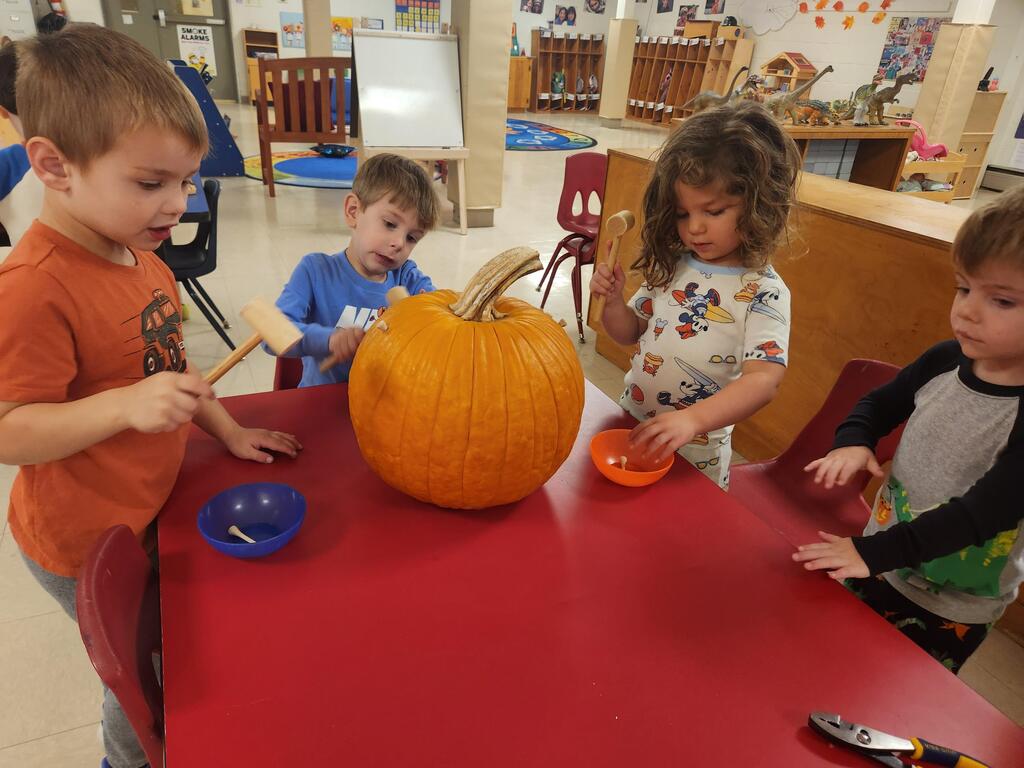 Four Kinderfolkers are hammering golf tees into a pumpkin.